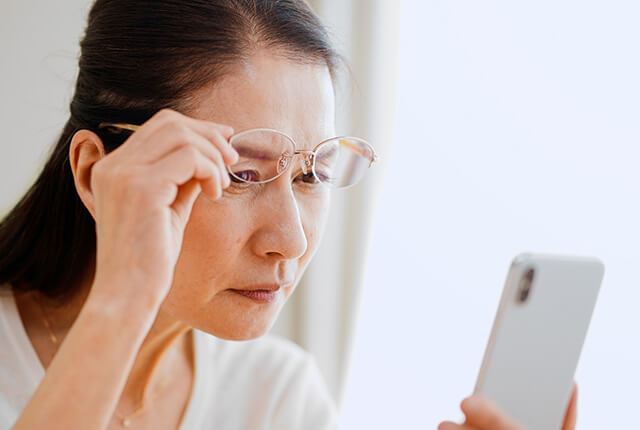 メガネを上に上げ携帯を見る高齢女性